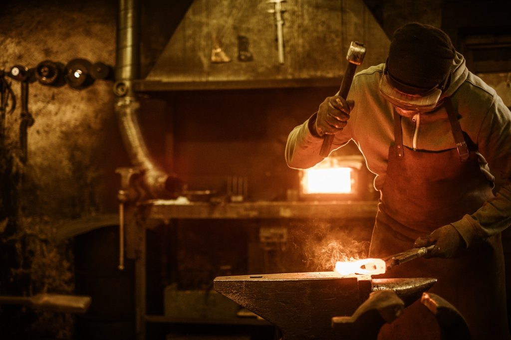 Blacksmith forging the molten metal on the anvil in smithy